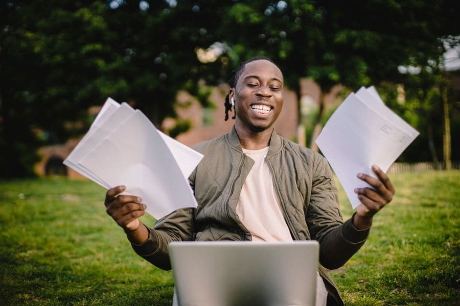 A smiling man holding up his documents beside a laptop