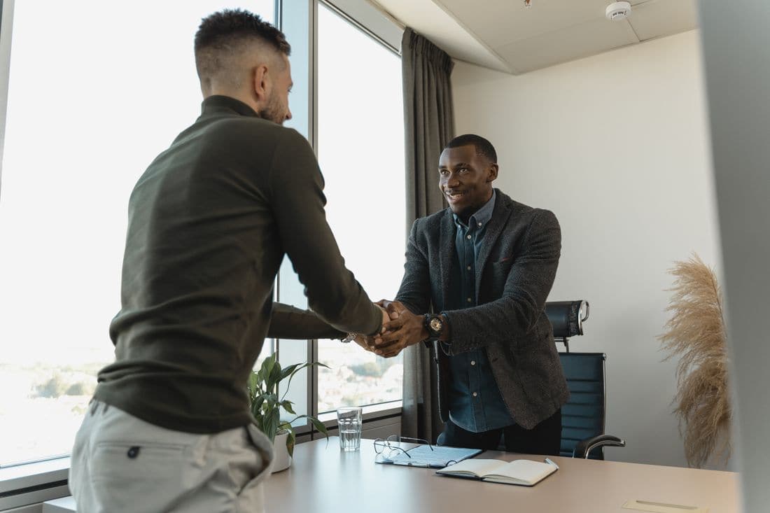 Two men shaking hands across a desk in an office